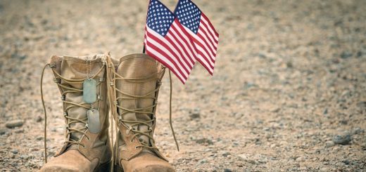 Old military combat boots with dog tags and two small American flags. Rocky gravel background with copy space. Memorial Day or Veterans day concept.
